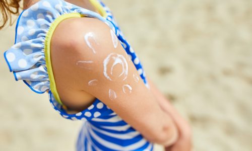 Little girl with applying sunscreen on shoulder in form of the sun standing on the beach, protection sun cream skin. Summer vacation.